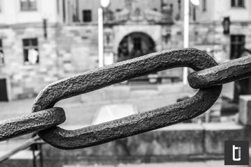 A close black and white photograph of a heavy metal chain link.