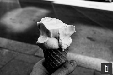 A black and white close photograph of an ice cream cone held in a hand.