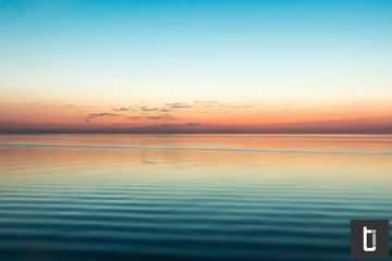 A calm sea at sunset with bands of soft pastel colour.
