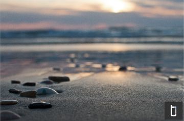 Low evening light over a quiet beach with soft waves and a muted horizon.